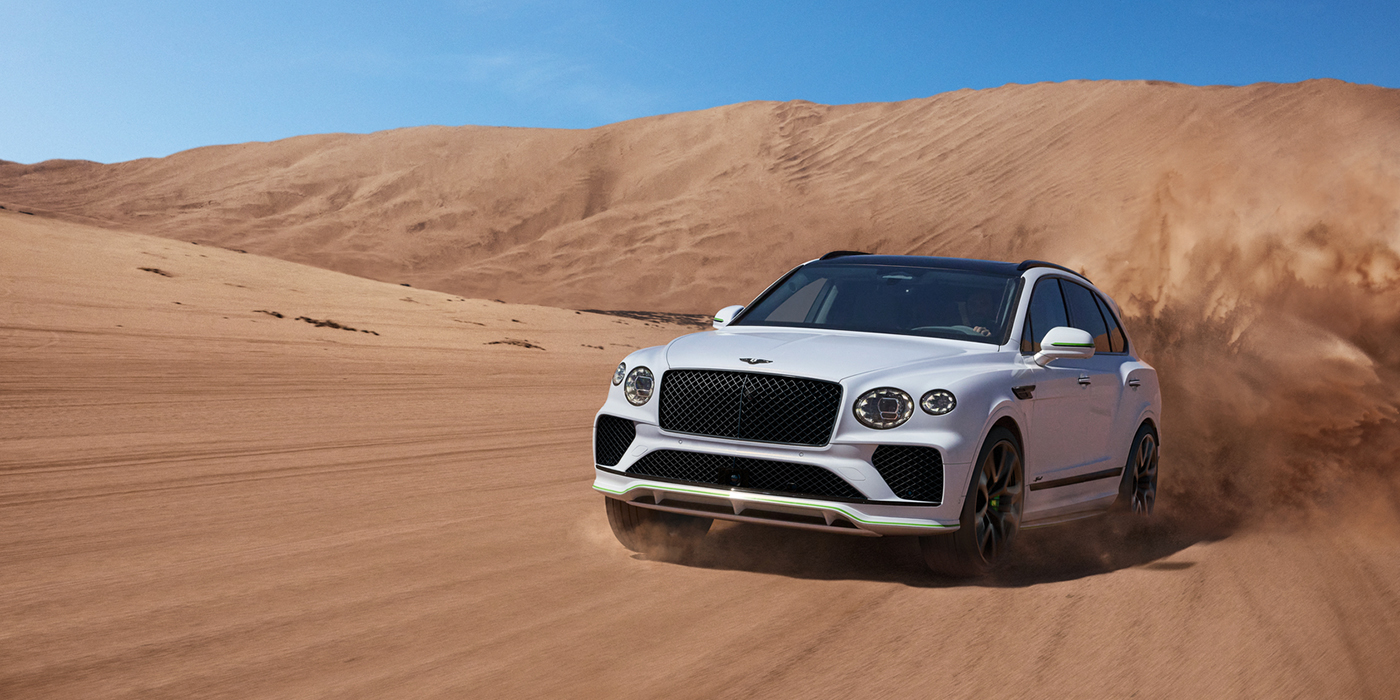 Bentley Bucuresti Bentley Bentayga Speed SUV front three quarter in Snow Quarts Pearlescent by Mulliner white paint driving dynamically through the desert