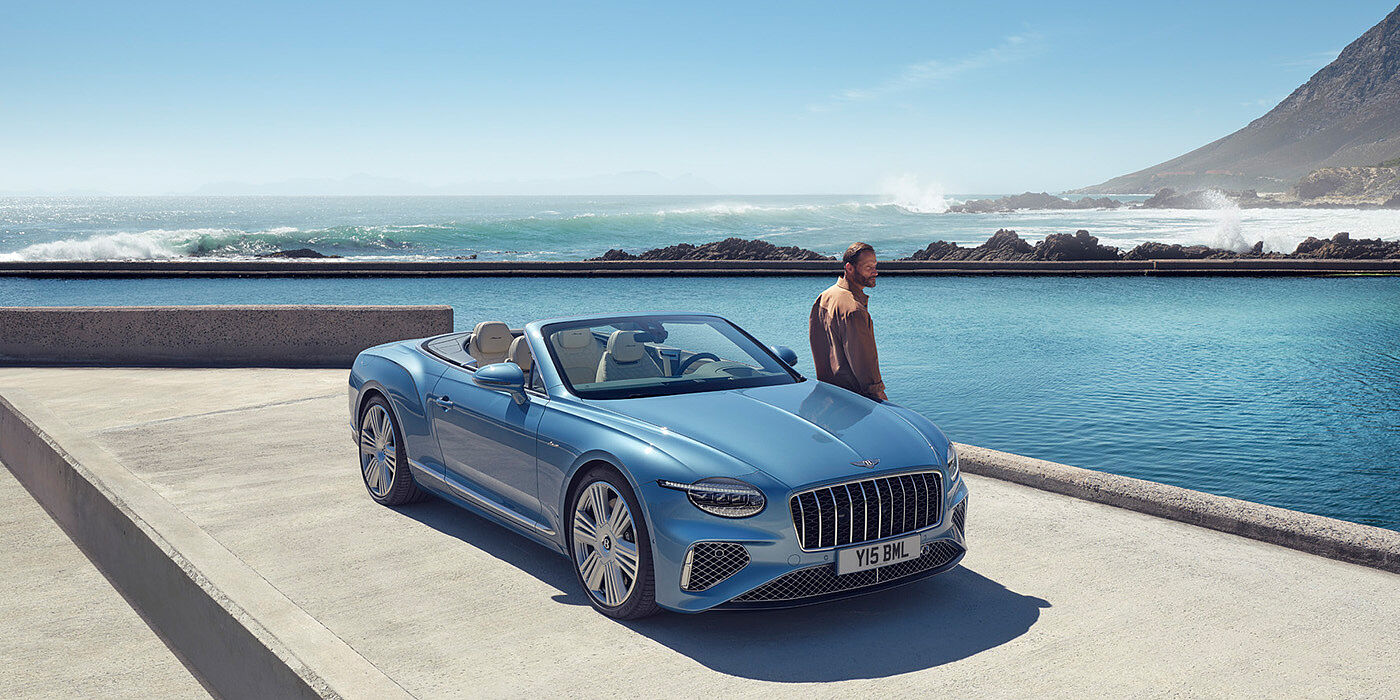 Bentley Bucuresti New Bentley Continental GTC Azure convertible front view in Light Windsor blue paint with 22 inch ten spoke wheels parked by the sea in the sunshine