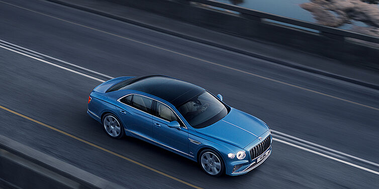 Bentley Bucuresti New Bentley Flying Spur Azure sedan in Light windsor blue paint by Mulliner, with 22 inch Azure wheels seen from overhead driving dynamically on a country road