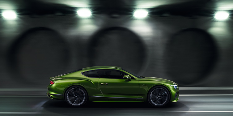 Bentley Bucuresti Bentley Continental GT Speed coupe profile in Tourmaline Green driving dynamically past a concrete wall at night