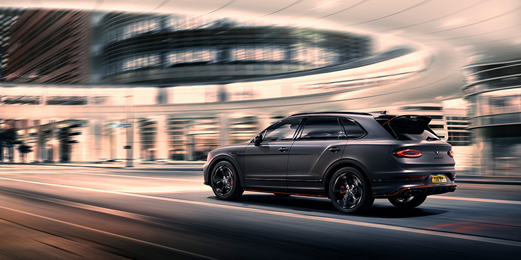 Bentley Bucuresti Bentley Bentayga S Black Edition SUV rear three quarter in Anthracite Satin paint driving dynamically through a city at night