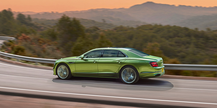 Bentley Bucuresti Bentley Flying Spur Speed sedan side profile in Tourmaline Green paint driving dynamically on a mountain road at sunset