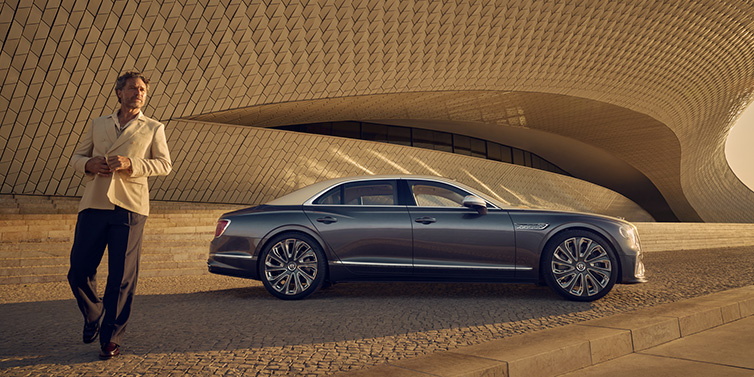 Bentley Bucuresti Bentley Flying Spur Mulliner sedan in Rose Gold over Magnetic duotone paint parked by a curved wall with person in suit jacket standing on the left