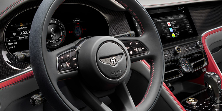 Bentley Bucuresti Bentley Flying Spur Speed sedan front interior detail showing steering wheel and driver screens surrounded with Hotspur red and Gravity Grey hides